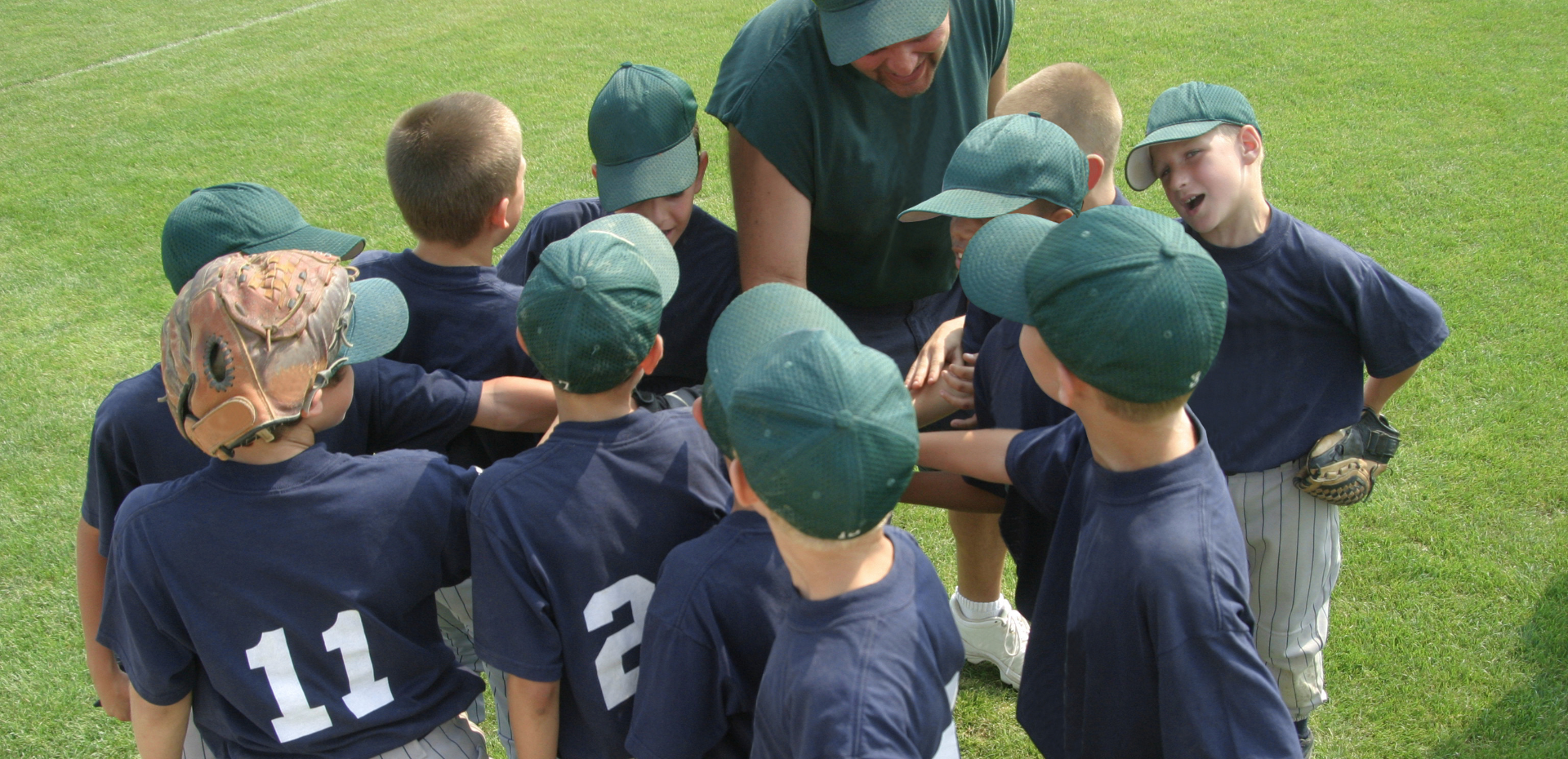 Baseball team huddled together on a field with a coach.